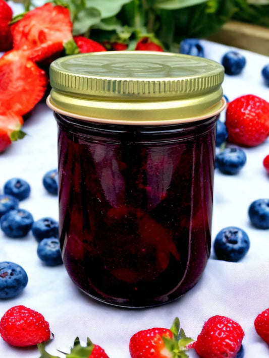 a jar of strawberry blueberry jam on a white tablecloth with fresh strawberries and blueberries surrounding it.