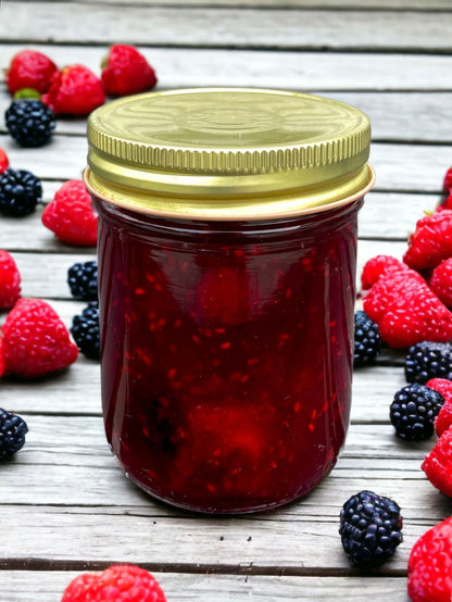 A jar of strawberry, raspberry, blackberry jam sitting on a rustic wooden table with fresh berries all around