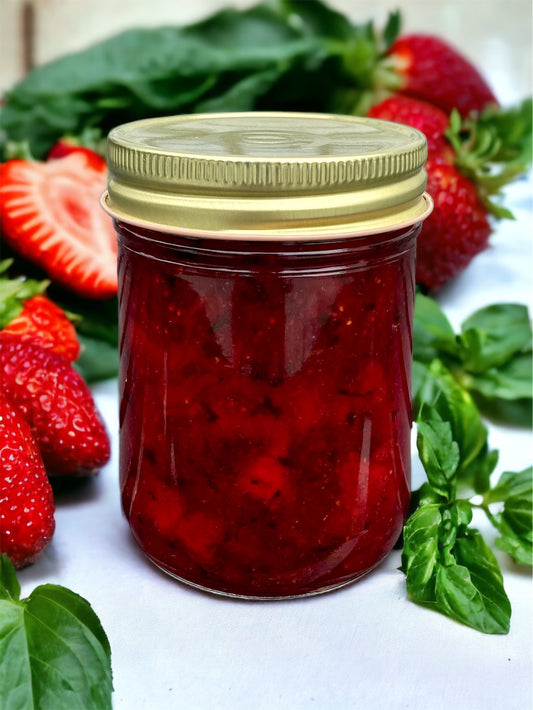 a jar of strawberry basil jam on a marble surface with fresh strawberries and basil in the background