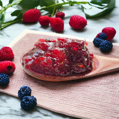 a wooden spoon loaded with jam made from strawberries, raspberries and blackberries resting on a linen towel with fresh berries in the background